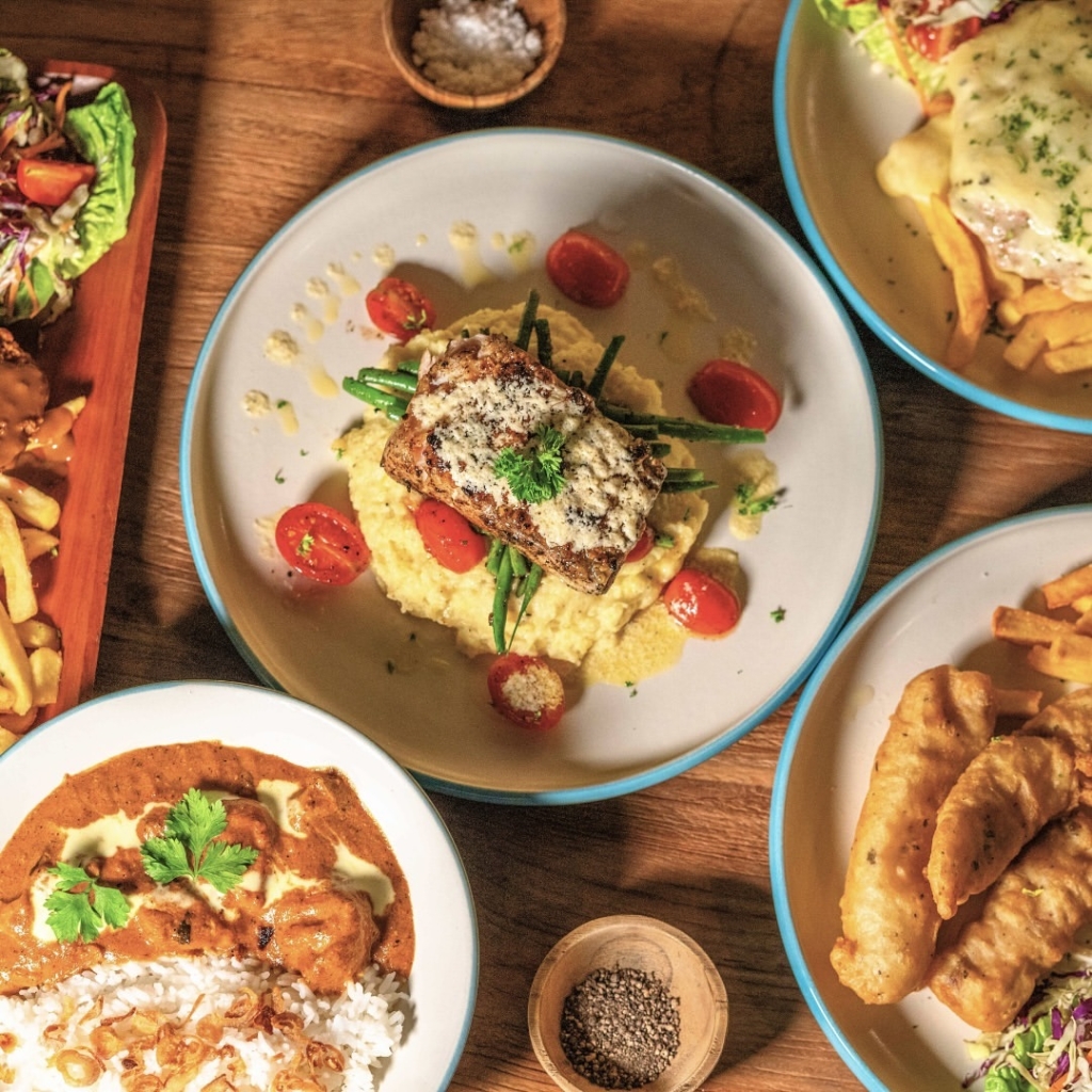 plates of different dishes, center is a plate of omelette with tomatoes on its side, and a piece of meat on top. 